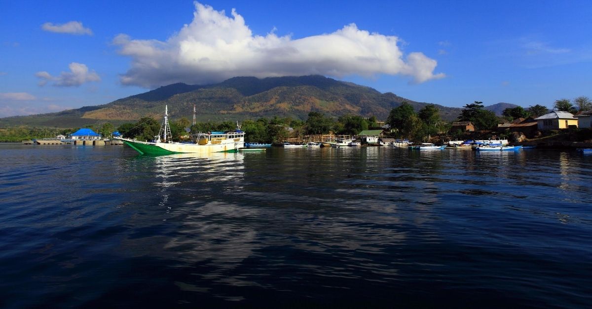 boats in harbor with mountainous island with large white cloud and blue sky