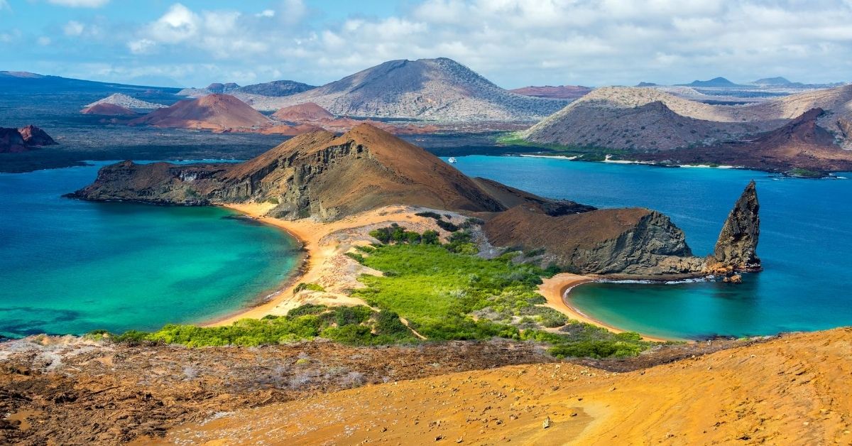 panoramic view from mountain down to peninsula with beaches on either side surrounded by aquamarine waters and mountains in the background