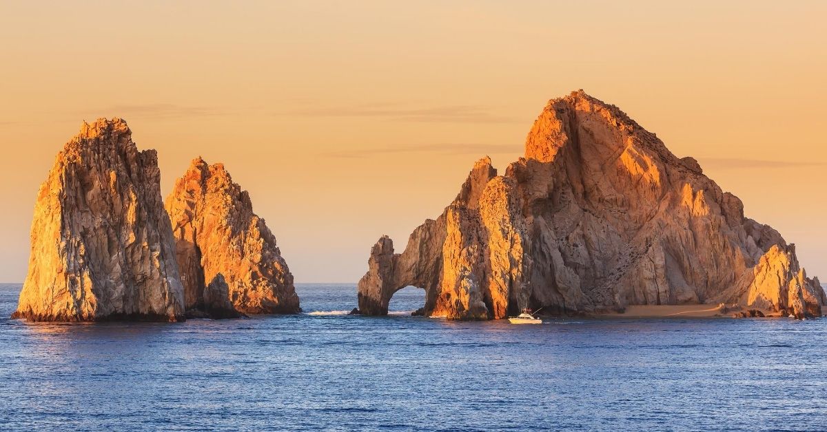 two huge rock formations in the sea with boat at dusk