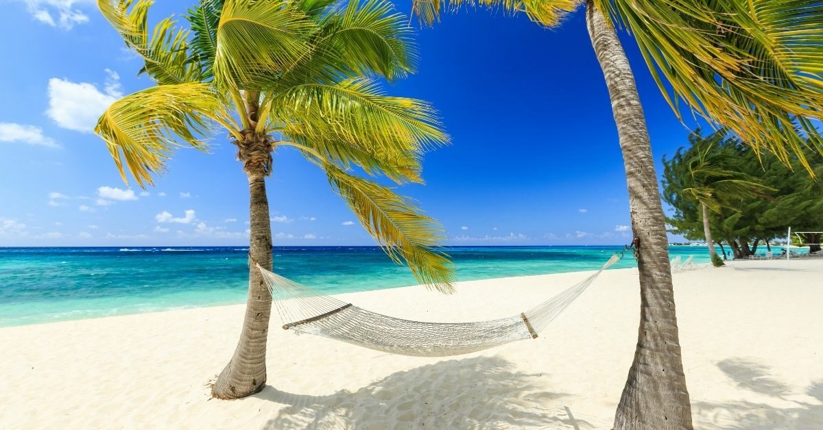 hammock hanging from two palm trees on a breezy beach with the Caribbean in aqua and blue waters of the Caribbean