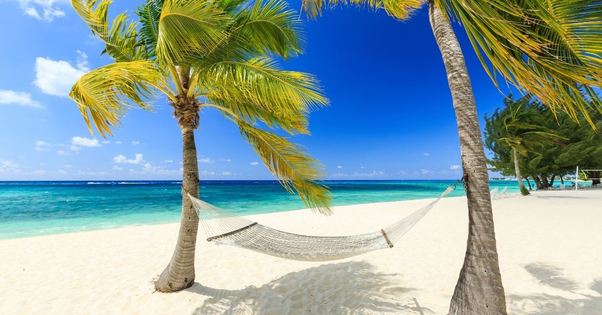 hammock hanging from two palm trees on a breezy beach with the Caribbean in aqua and blue waters of the Caribbean
