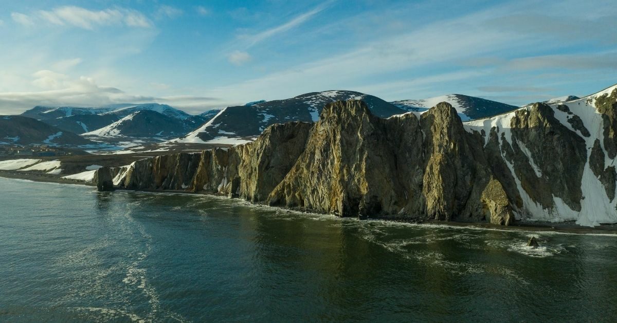 Mountains with snow and cliff faces in the Siberian coast with cloudy, light blue sky