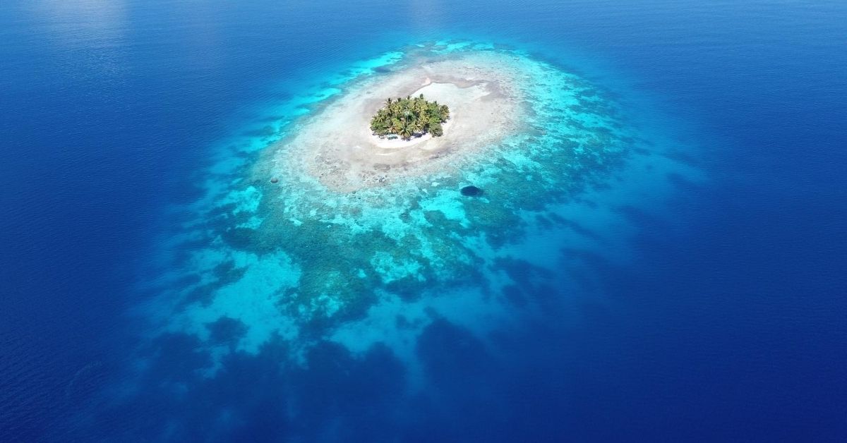 aerial view of tiny palm covered island surrounded by coral and the Pacific