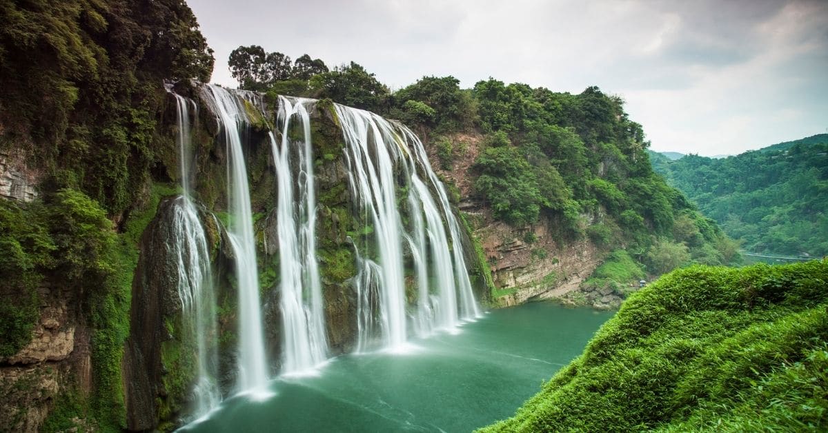 stunning waterfalls empty into a aquamarine river in a mountainous area