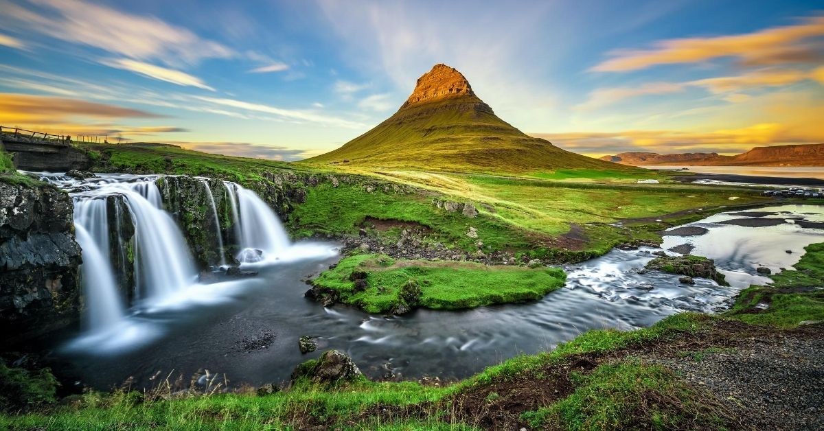 stunning waterfall with three cascades at Kirkjufellsfoss at dusk with dramatic sky and cone shaped mountain