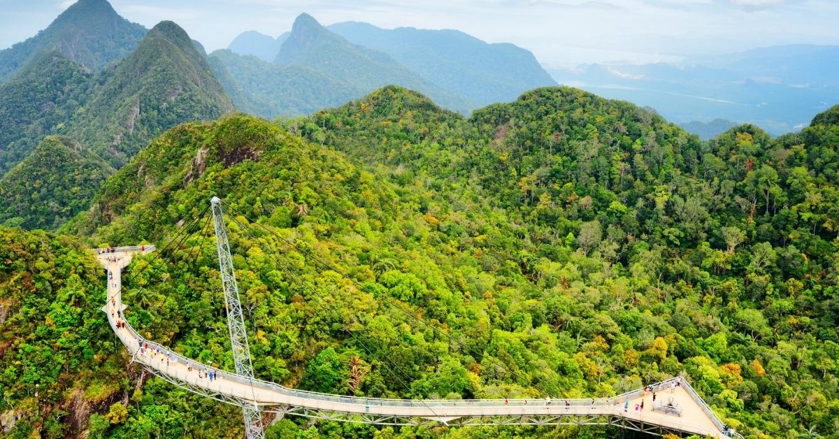 mountain peaks covered with trees and a meandering pedestrian bridge