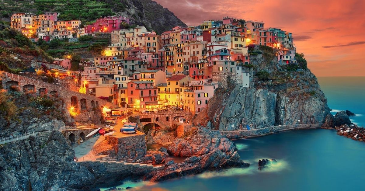 colorful village atop a mountain cliff along the coast at sunset with houses illuminated
