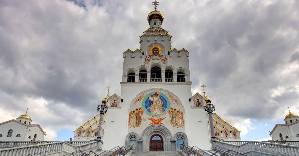 white church with colorful and ornate religious art depicted on building against a cloudy sky