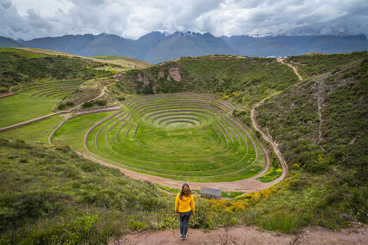 girl standing before circle terraces at the Inca archaeological site of Moray in Peru