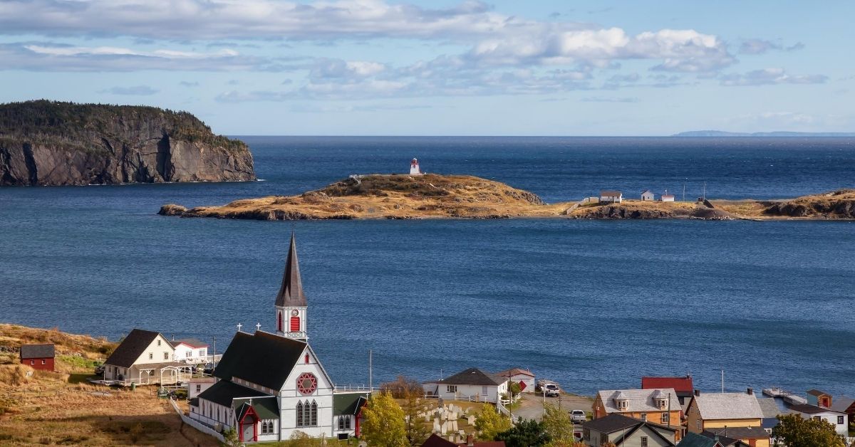 coastal fishing village with white and red church and Atlantic ocean on sunny, cloudy day