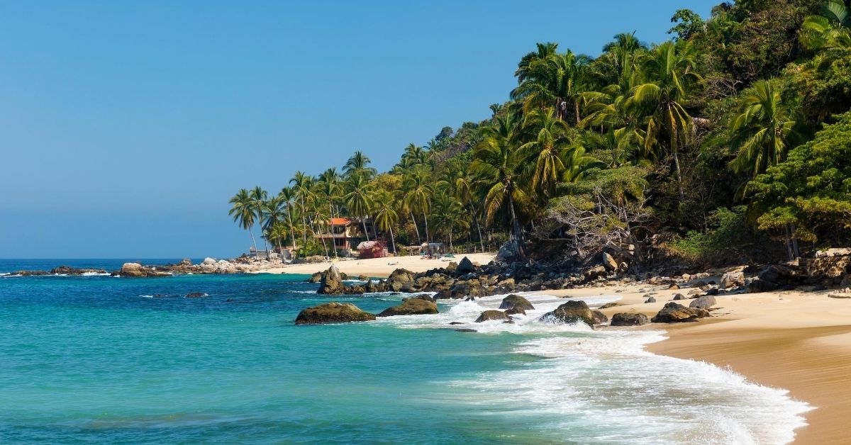peaceful beach with palm trees, rocks and house in the distance