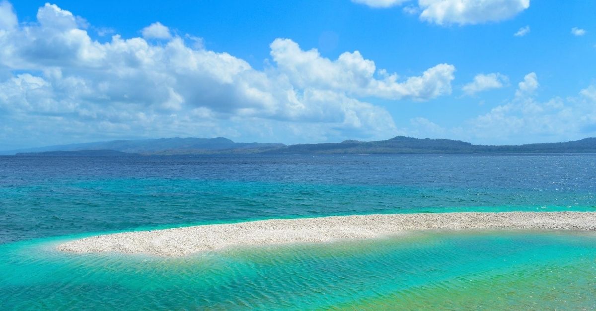 sand bar surrounded by azure waters and mountains in the background