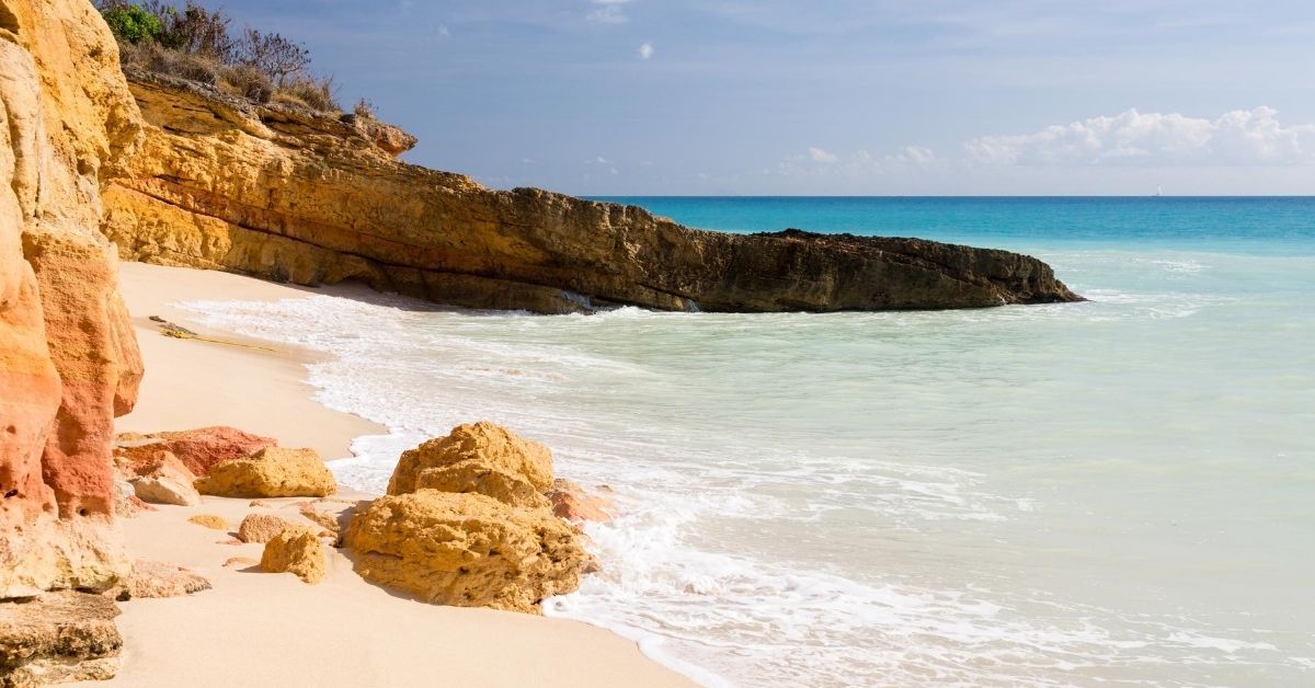 beach at the base of a cliff with Caribbean and rocks