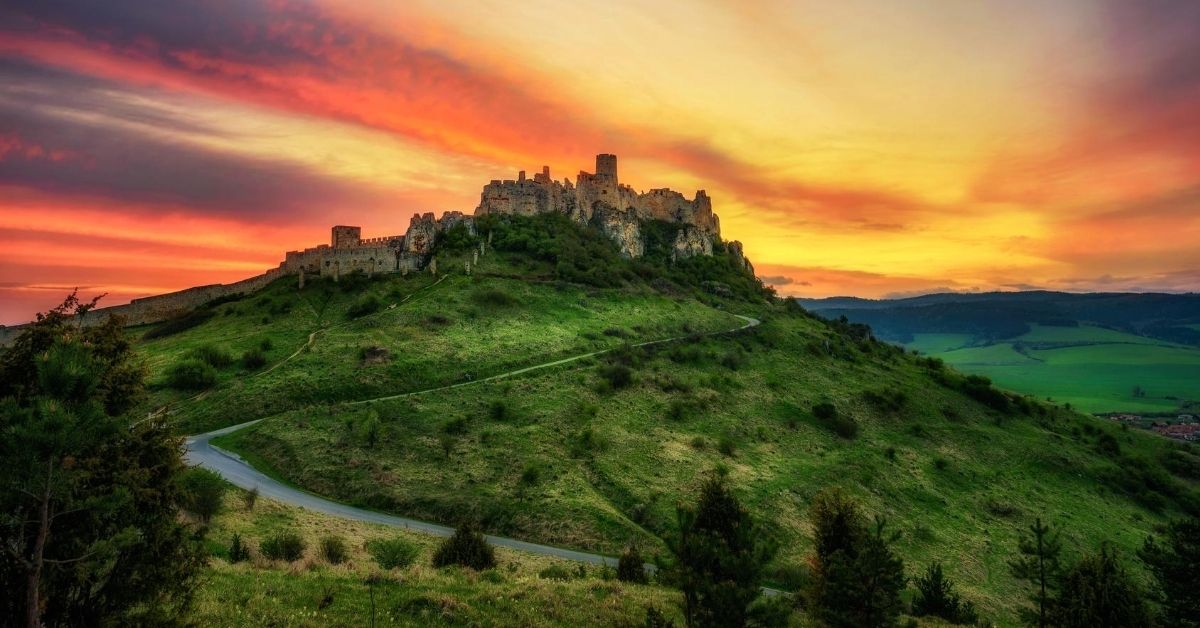 castle on a green hill with fiery sunset overlooking valley below
