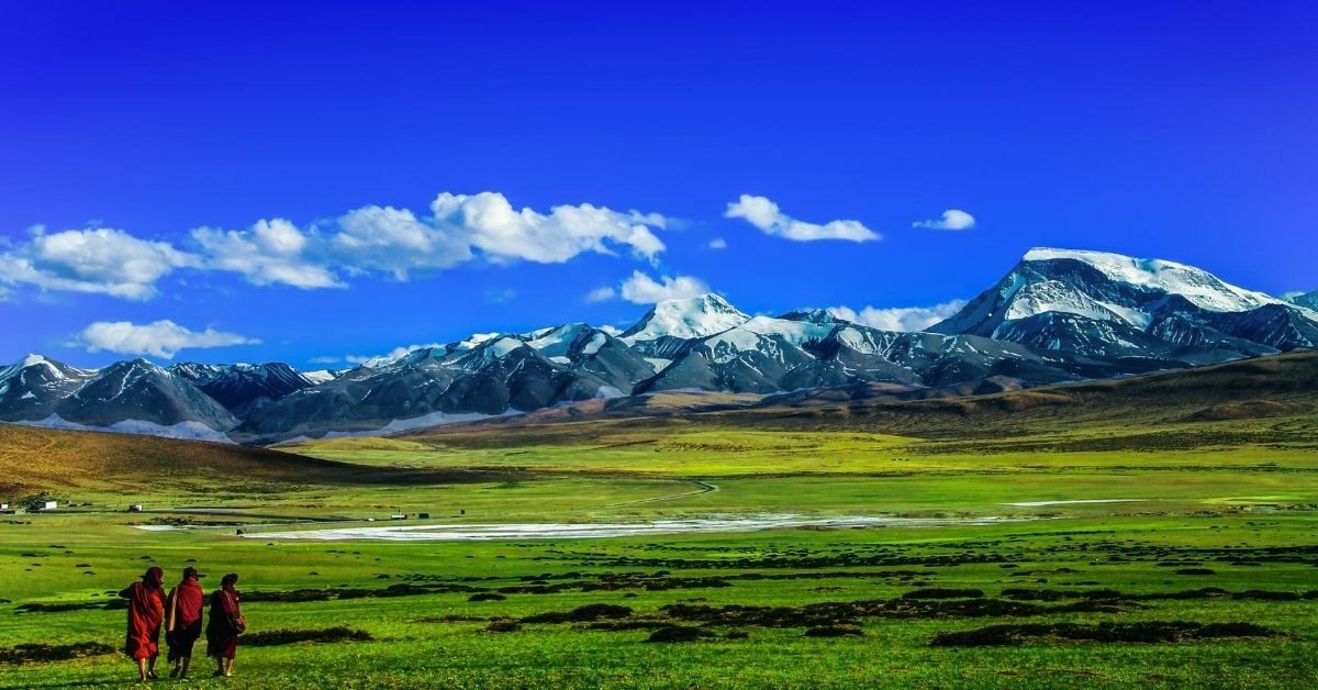 monks walking in vast green landscape with snow capped mountain range in Tibet