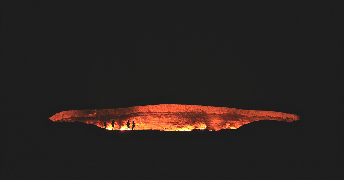 fire in natural gas crater at night with people standing at the edge in silhouette