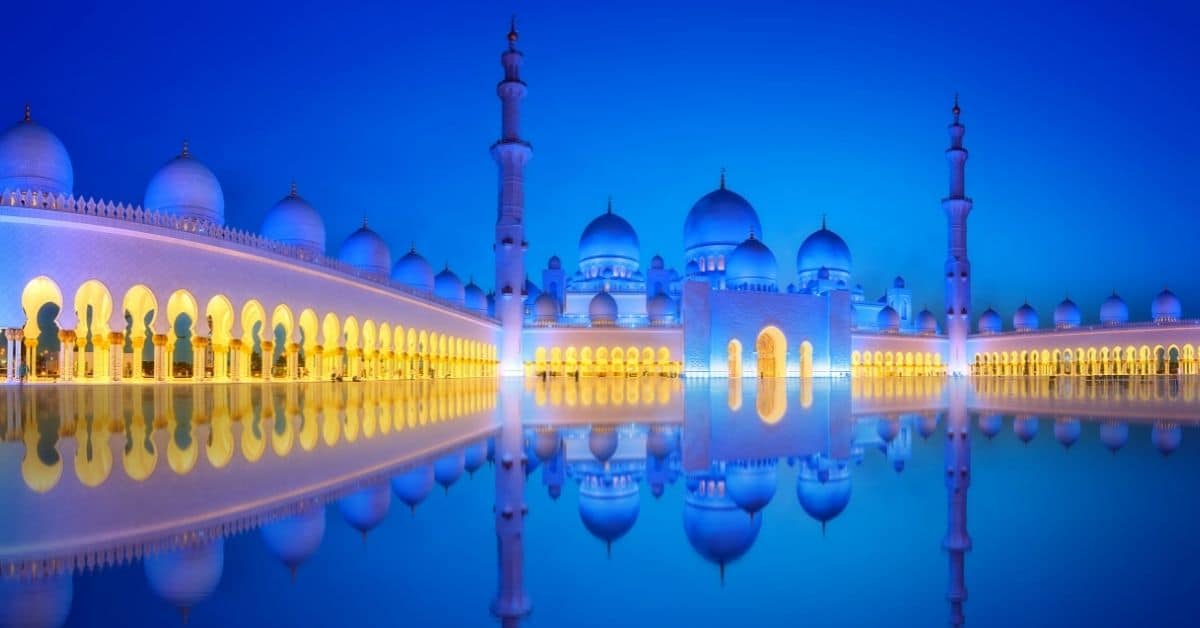 A beautiful white mosque in Abu Dhabi with a reflecting pool at night is glowing