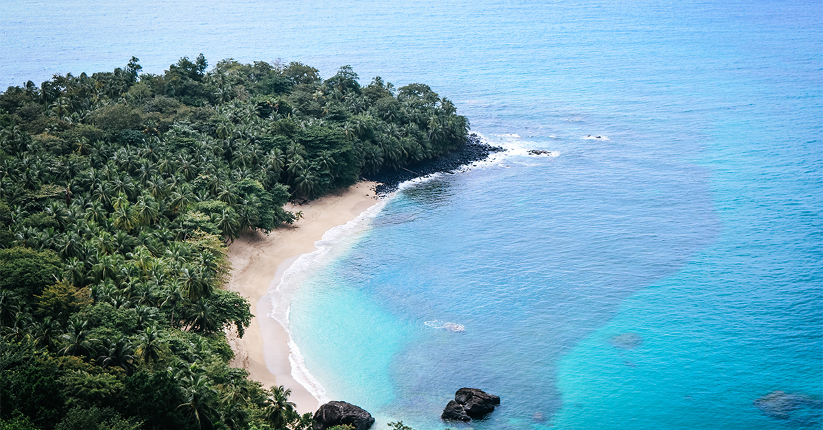 lush jungle and banana shaped beach with shades of blue and turquoise waters in São Tomé & Príncipe