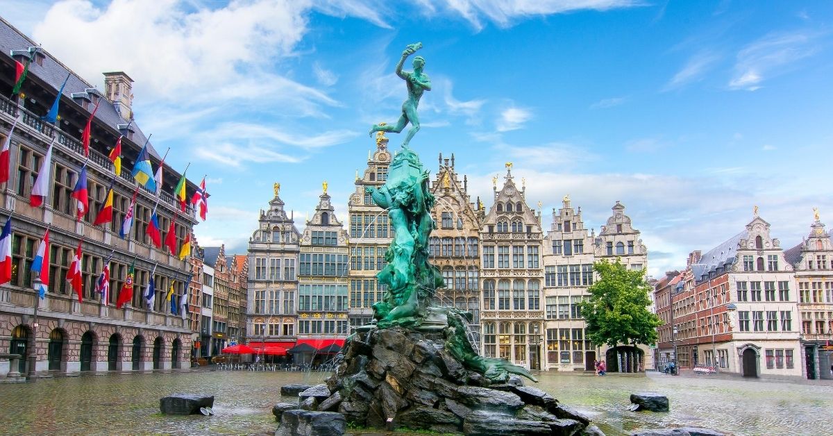 colorful flags and buildings in square in Antwerp with fountain on a bright, cloudy day