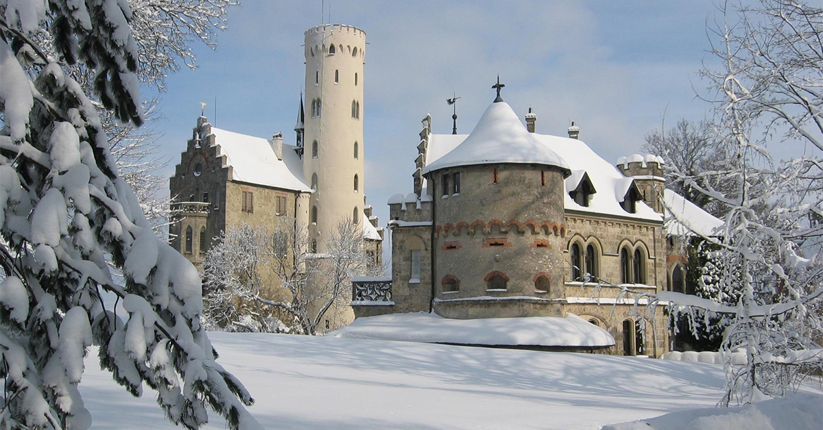 light colored castle in Liechtenstein with snow covered ground and trees with cloudy blue skies