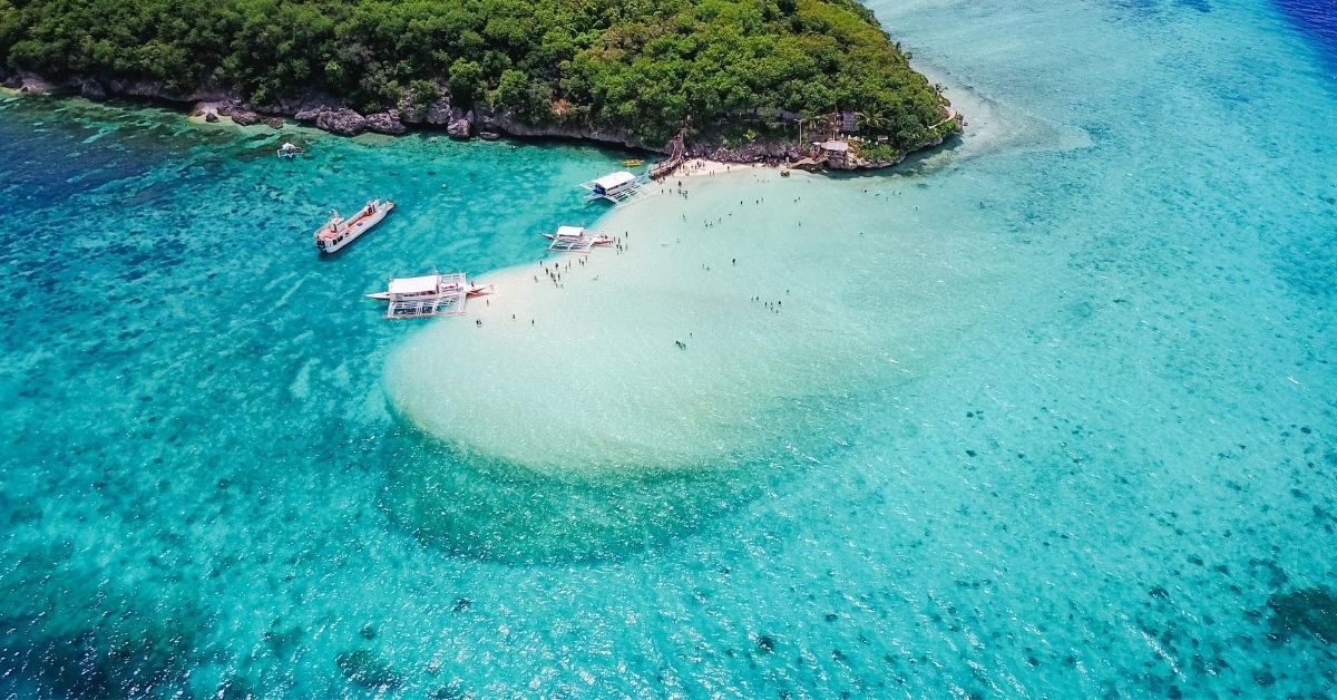 boats perched on sandbar off Cebu with stunning turquoise water surrounding green island
