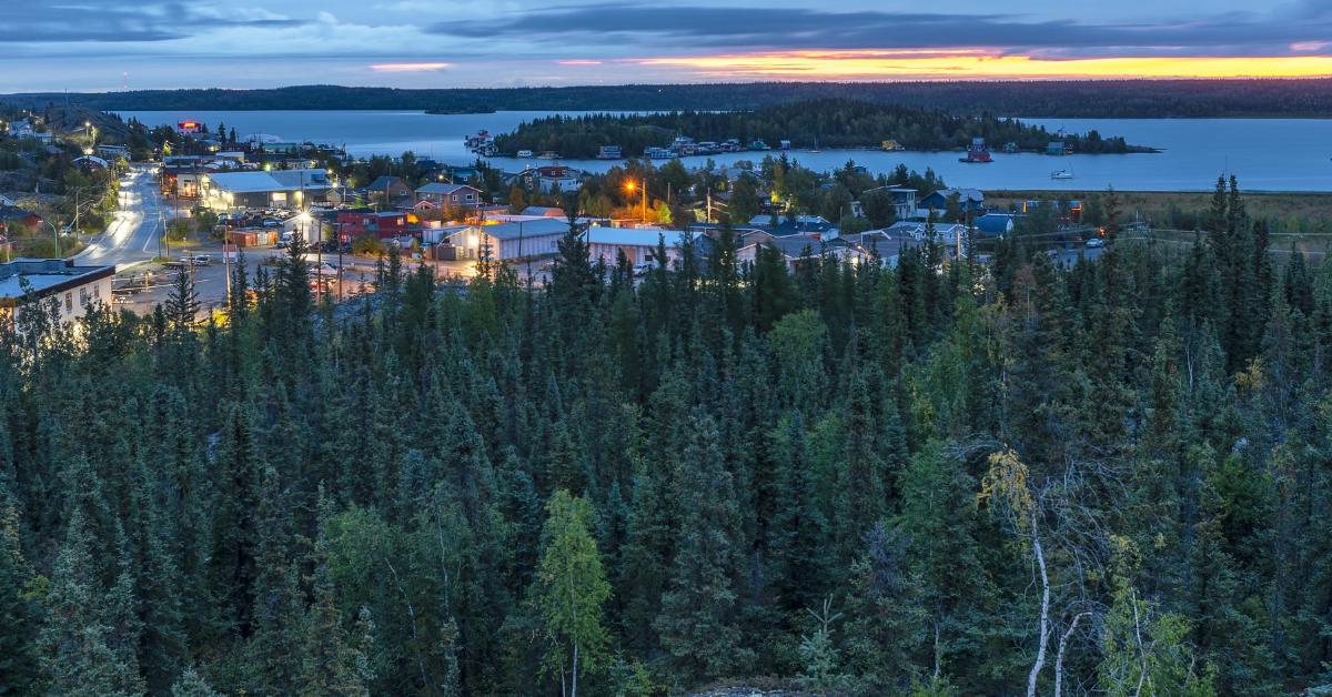aerial view of trees and town of Yellowknife with surrounding lake illuminated by streetlights at dusk