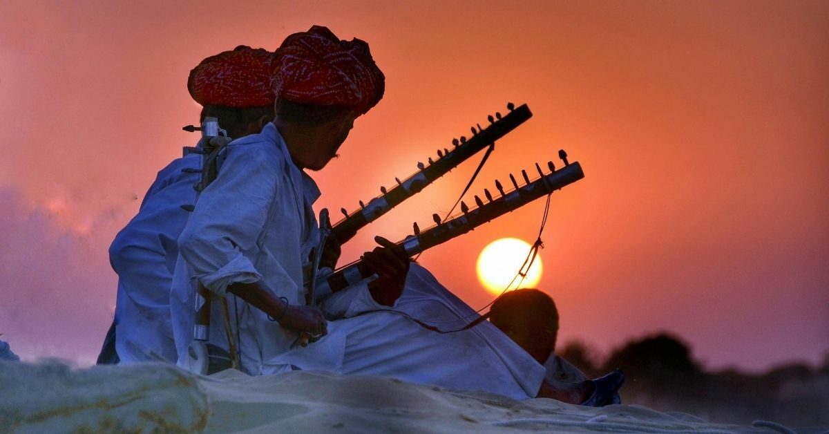 2 men playing sitars with an orange sunset behind