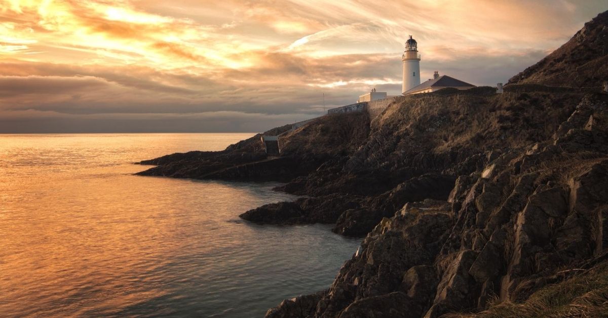 white lighthouse atop a cliff with orange clouds at sunset