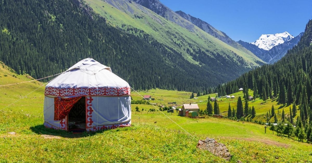 white and red yurt in rural mountain valley with small village during summer in Kyrgyzstan