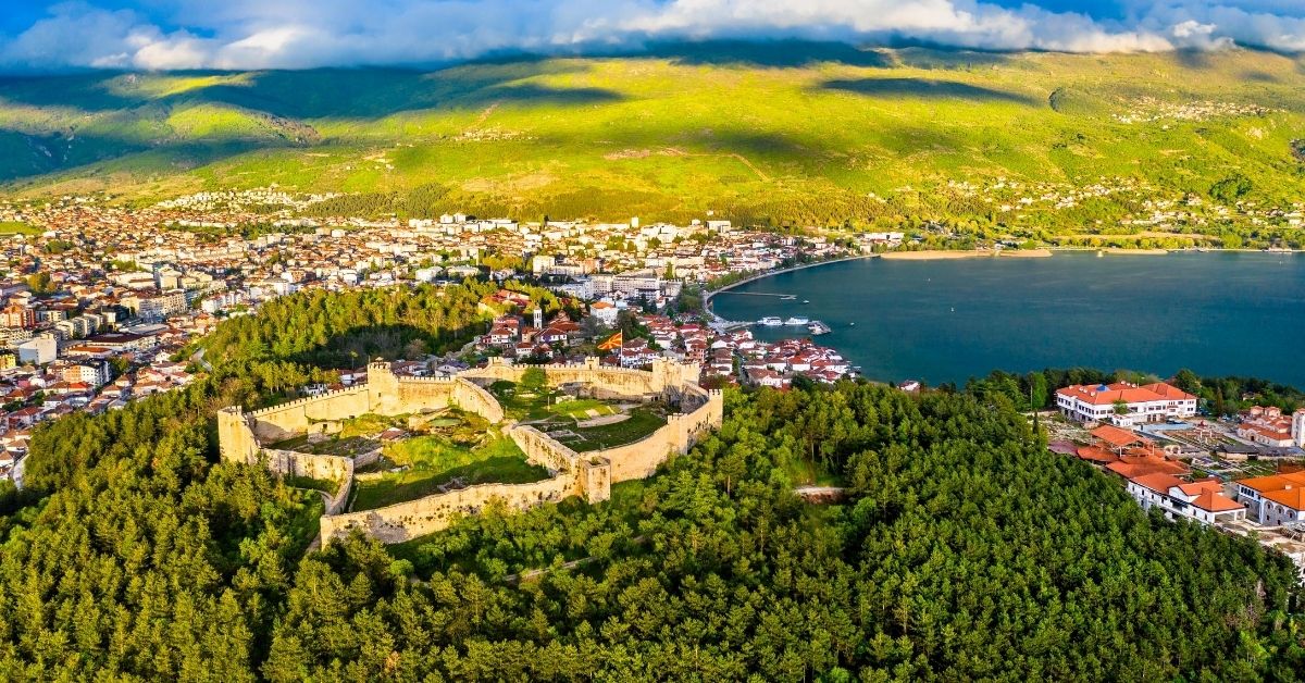 aerial of fortress and surrounding forest, mountains and city of Ohrid in a bright cloudy day