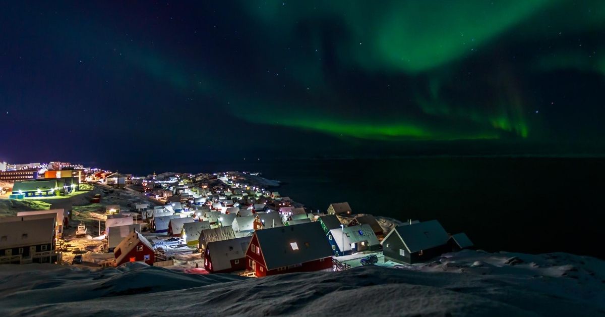 view down to a colorful village with the Northern Lights overhead