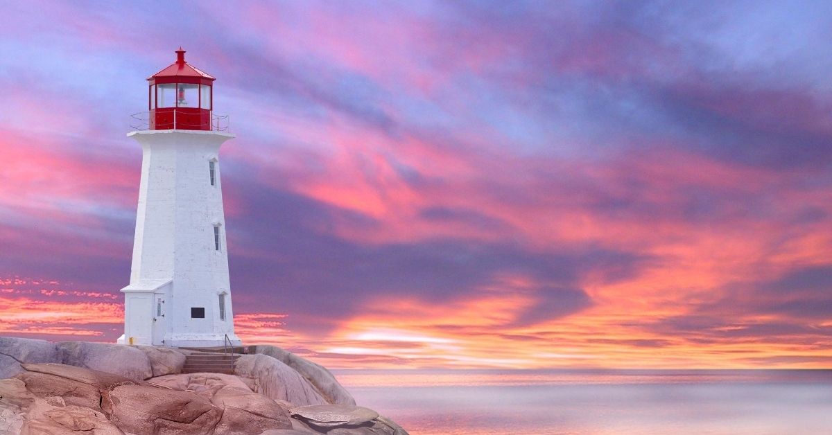white and red lighthouse atop rock hill on the coast of Nova Scotia