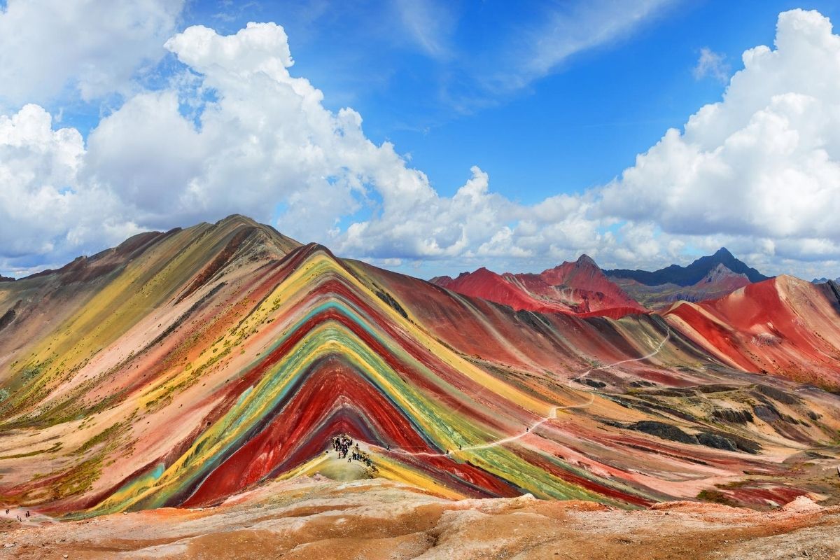 landscape with multicolored high altitude mountain range and tourists on a sunny, but cloudy day