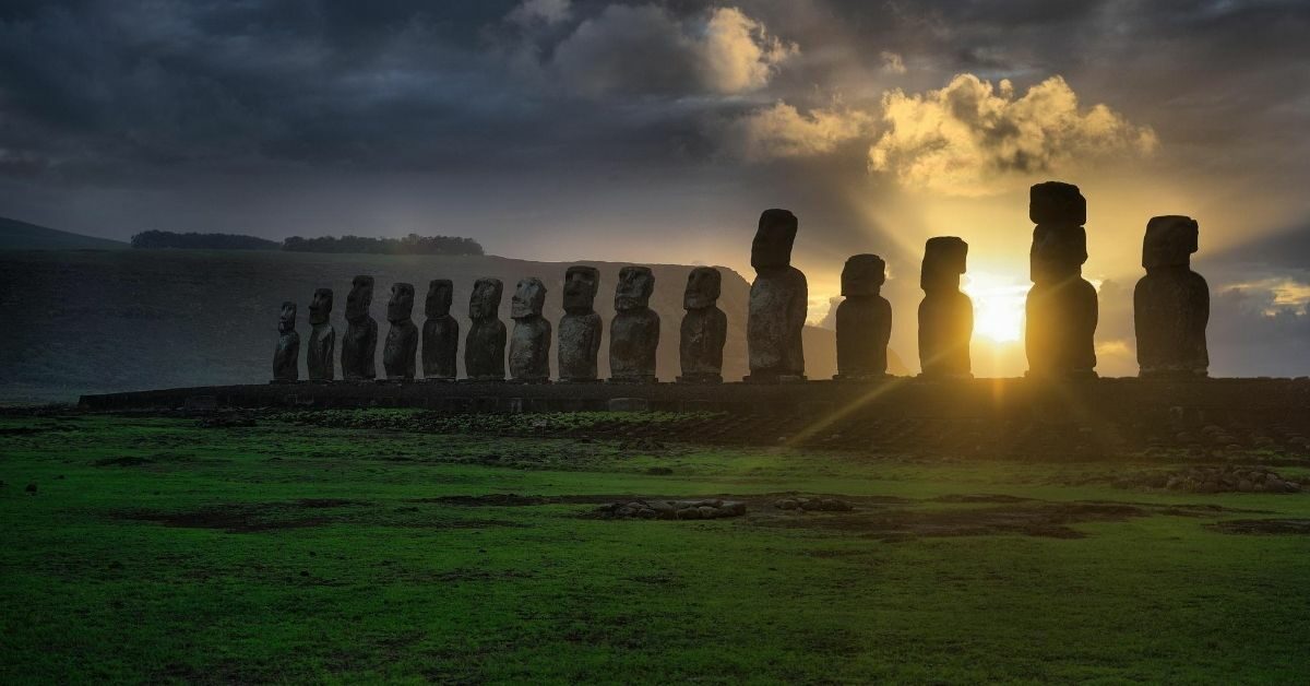 stone figures on Easter Island at dawn with sun rays shining through and cloudy dark sky