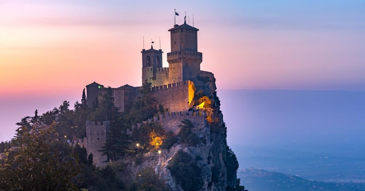 fortress perched and built into a rocky mountain overlooking valley below with pastel skies at dusk