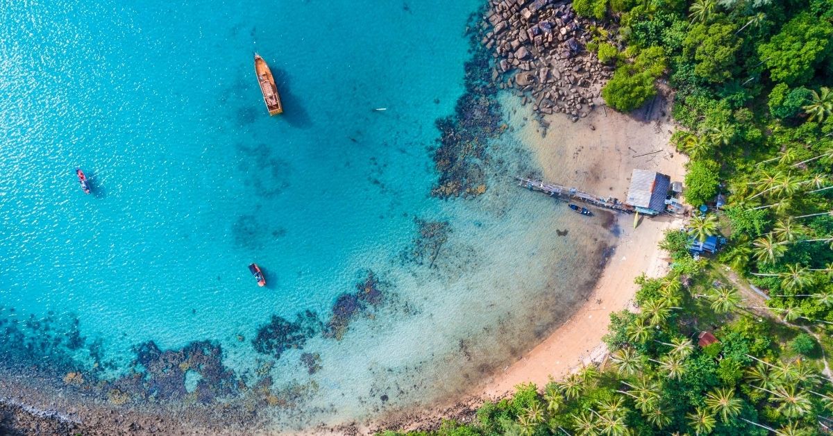 Blue turquoise water of the Indian Ocean with beach and green trees and palms